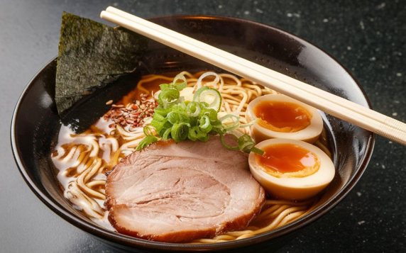 검은 그릇에 일본식 라면과 돼지고기 반숙계란 얇게 썬 대파등이 있다.