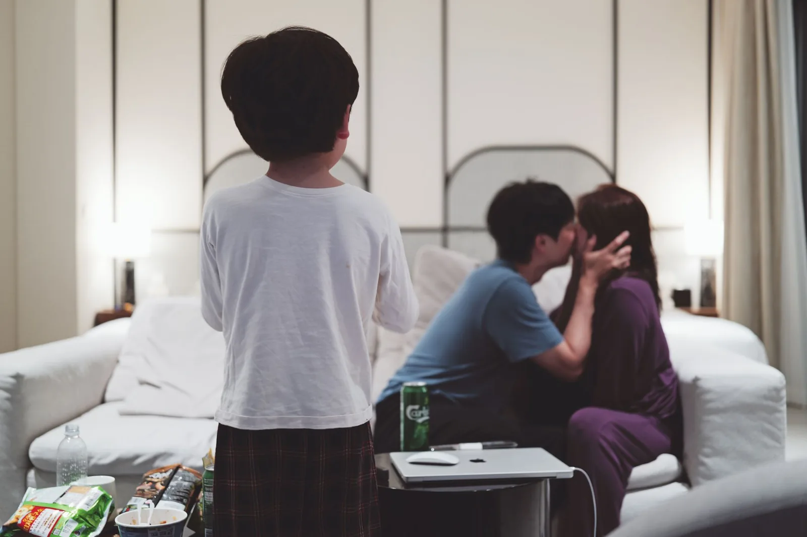 아늑한 저녁 시간, 한 쌍의 커플이 소파에서 시간을 함께 보내고, 그 앞에 아이가 서서 간식을 먹고 있습니다.