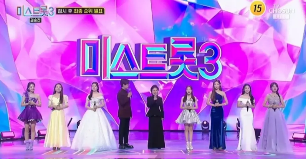 미스트롯 3-
보라색 배경 위 무지개색 글씨 미스트롯3
앞 최종 top7명 가운데 진행자와 가수 이미자가 서있는 모습