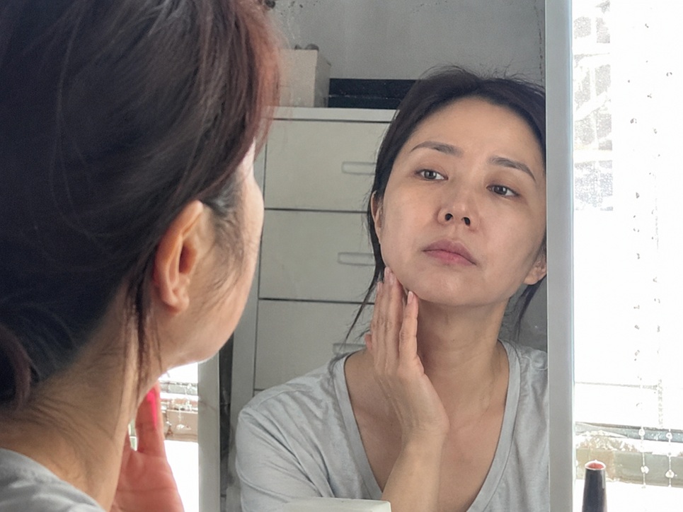 40대 여성이 화장대 거울을 보며 턱선을 만지고 있는 자연스러운 모습
