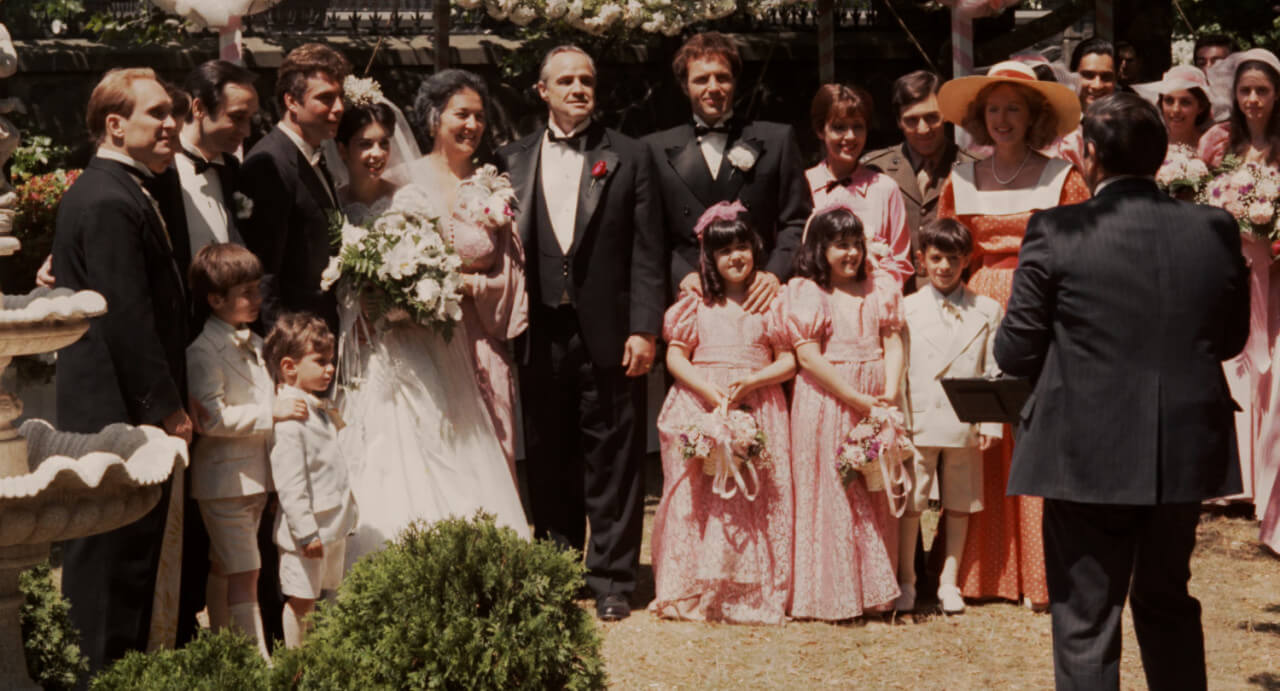 영화 도입부의 행복한 가족의 모습을 보여주는 딸의 결혼식에서 함께 사진찍는 꼴레오네 가의 가족들