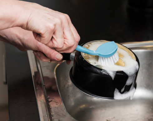 손으로 냄비 바닥의 탄 자국을 솔로 문질러 세척하고 있는 모습