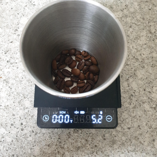 저울 위에 있는 메탈컵 속에 커피 원두가 담겨있다. 저울은 5.2g을 가르키고 있다.