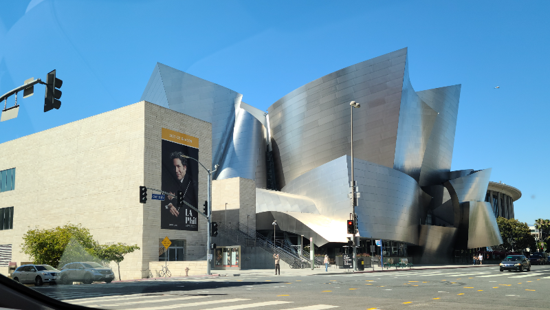 월트 디즈니 콘서트 홀. 마치 거대한 은색의 종이를 여러 개 말아 놓은 듯한 모양을 하고 있다. 왼쪽의 작은 건물 외벽에는 LA 필하모닉의 상임 지휘자인 구스타보 두다멜의 포스터가 걸려 있다.