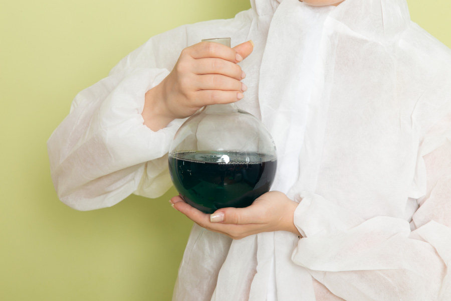 실험복을 입은 한 여성이 투명한 용기에 검은 난유를 반쯤 채운 것을 양쪽 손으로 들고 있는 것을 찍은 사진