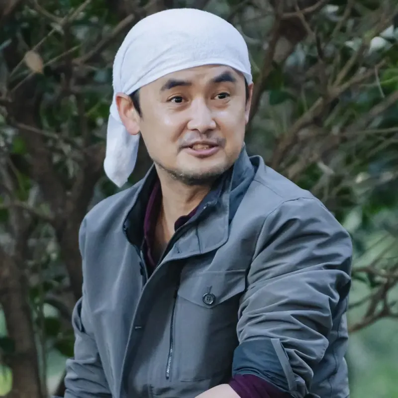 어느 나무를 배경으로 머리에 수건을 둘러쓰고 작업복을 입고 있는 드라마 이 연애는 불가항력의 나중범 캐릭터