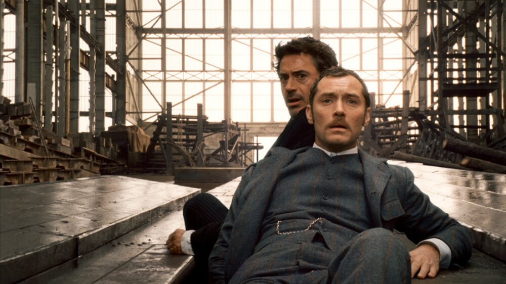 영화 셜록 홈즈 스틸컷 – 산업 현장 안에서 홈즈와 왓슨이 긴장감 속에 정면을 바라보는 하이라이트 장면
