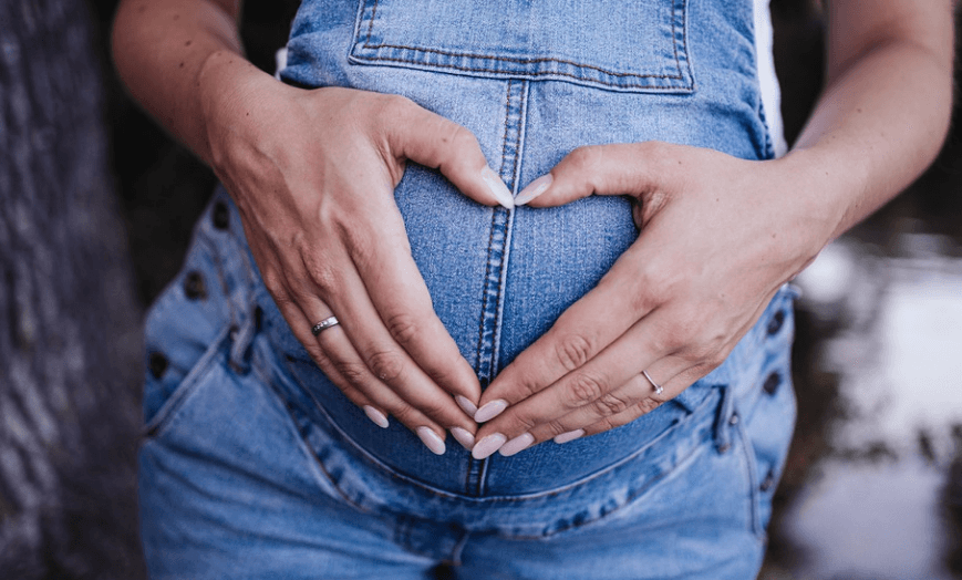 임산부가 자신의 배위에 손으로 하트 모양을 만들고 있다