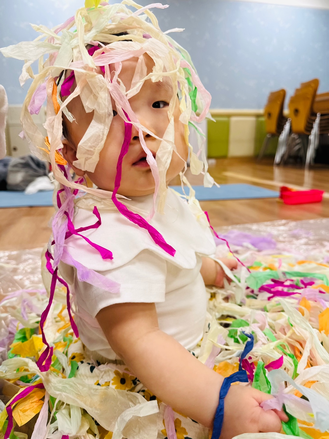 습자지를 손에 들고 머리와 어깨 위에 올려진 채 감각 놀이 중인 9개월 아기