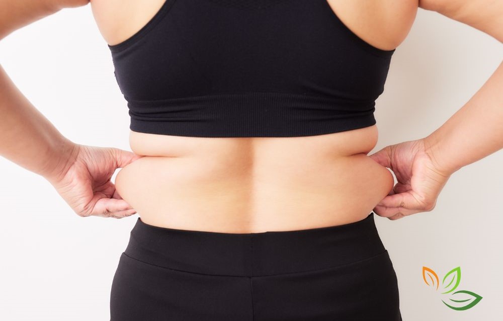 중년 여성이 복부 지방을 손으로 잡고 있는 모습, 중년 다이어트와 뱃살 관리의 필요성을 보여주는 이미지 via canva