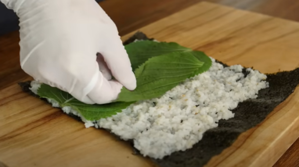 김에 밥을 올린 후 그 위에 깻잎을 올리고 있습니다 