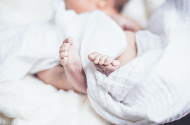 하얀 천 속에서 발을 내민 신생아의 작은 발, 따뜻한 조명 아래 평화롭게 잠든 아기