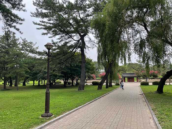 미추왕릉으로 가는 산책로에 탐방객이 미주왕릉 주변 풍경을 배경으로 사진을 찍고 있는 사진