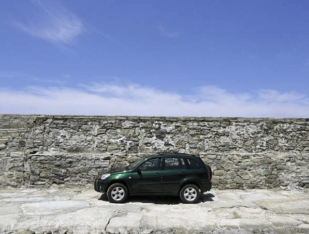 중고차 수출용 녹색 SUV 차량이 바닷가 바위 앞에 주차되어 있는 모습