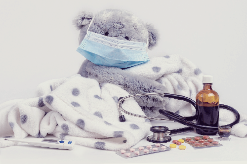 마스크를 쓰고 담요를 덮고 있는 회색 곰돌이 인형 사진