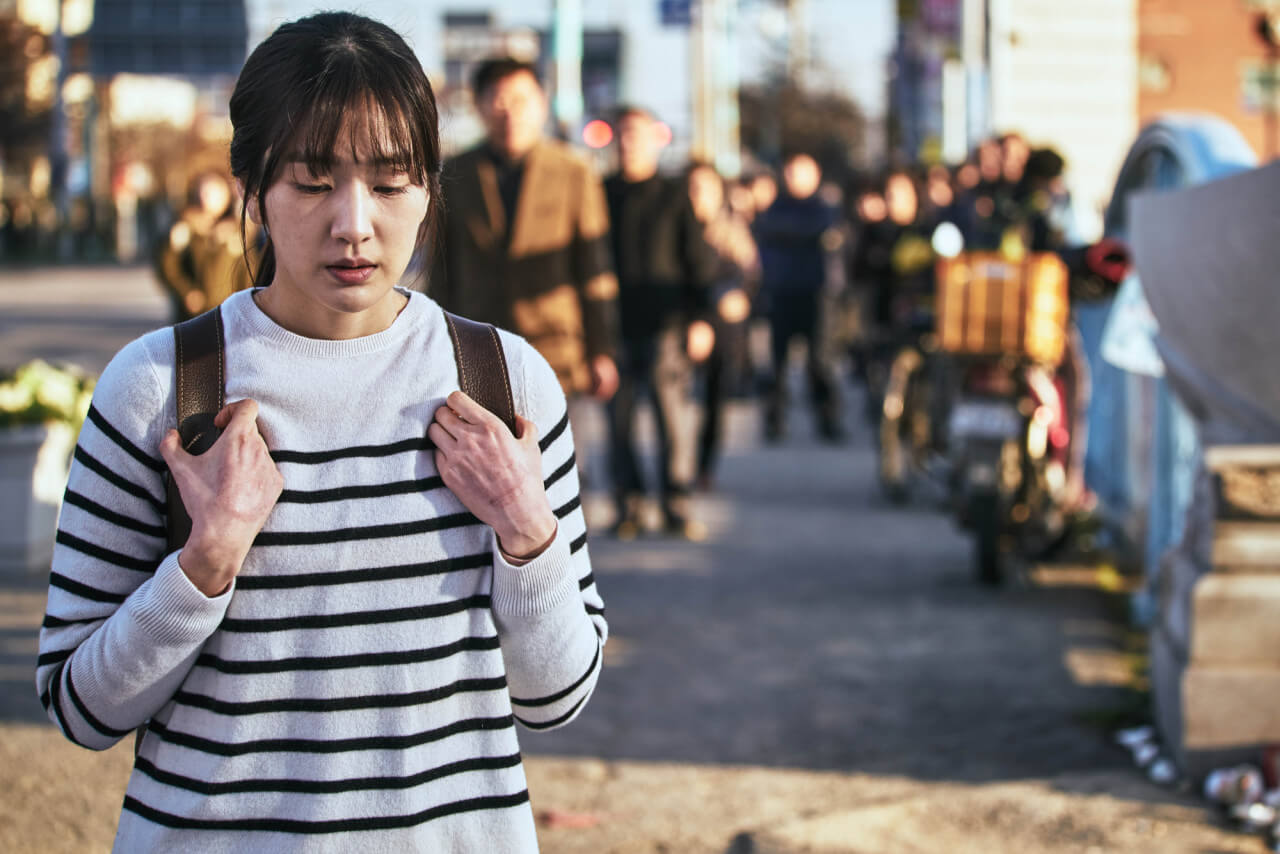 백 팩 가방 끈을 부여잡고 아래를 보며 걷는 불안해 보이는 여자