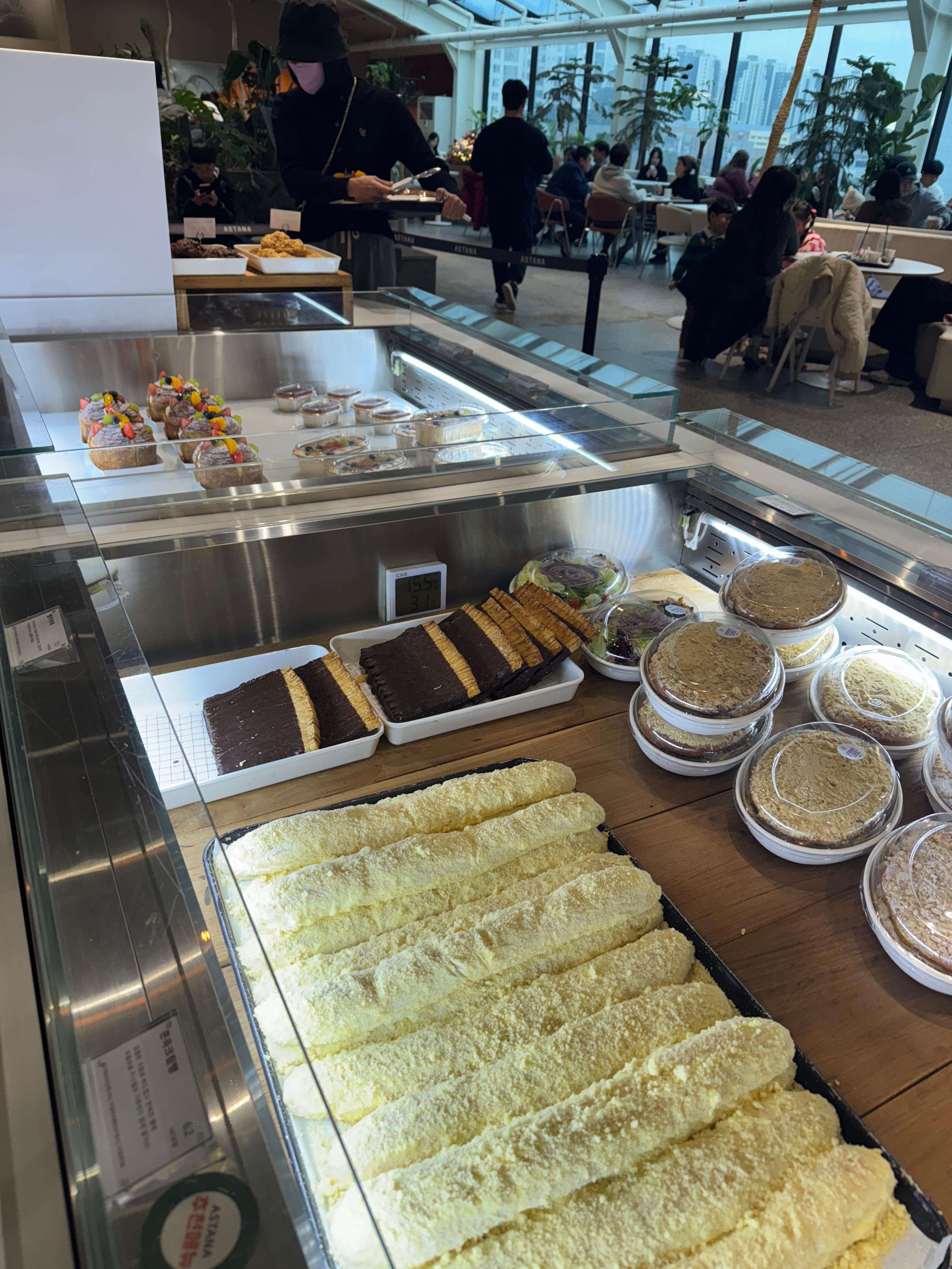동탄 카페 아스타나 내부와 디저트 쇼케이스&amp;#44; 케이크와 파운드 디저트가 진열된 냉장 쇼케이스 뒤로 좌석이 가득 찬 카페 분위기