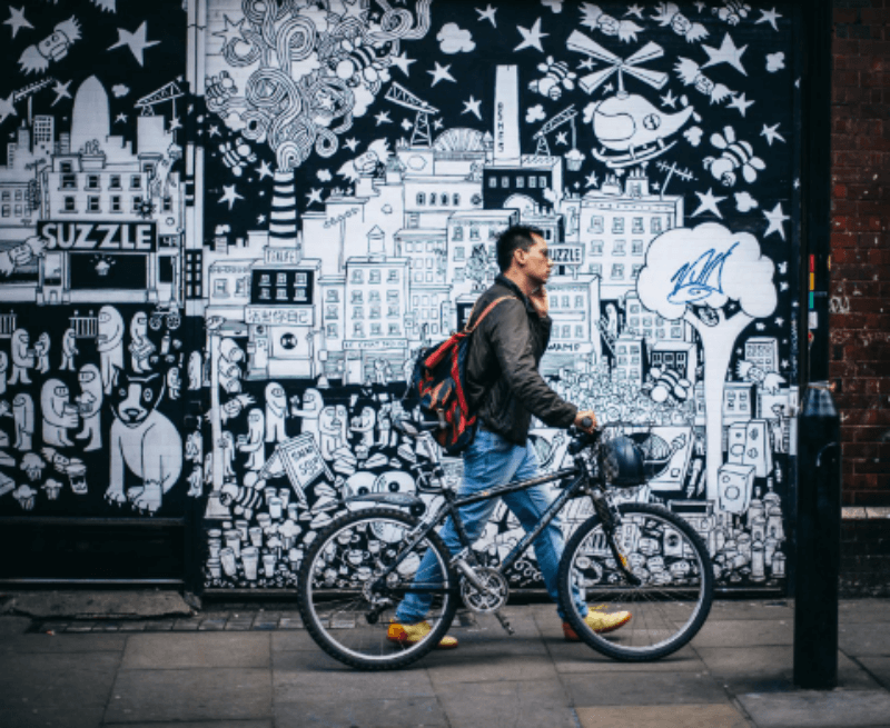 자전거를 끌고 전화를 하면서 벽화 옆을 지나가는 남자 사진