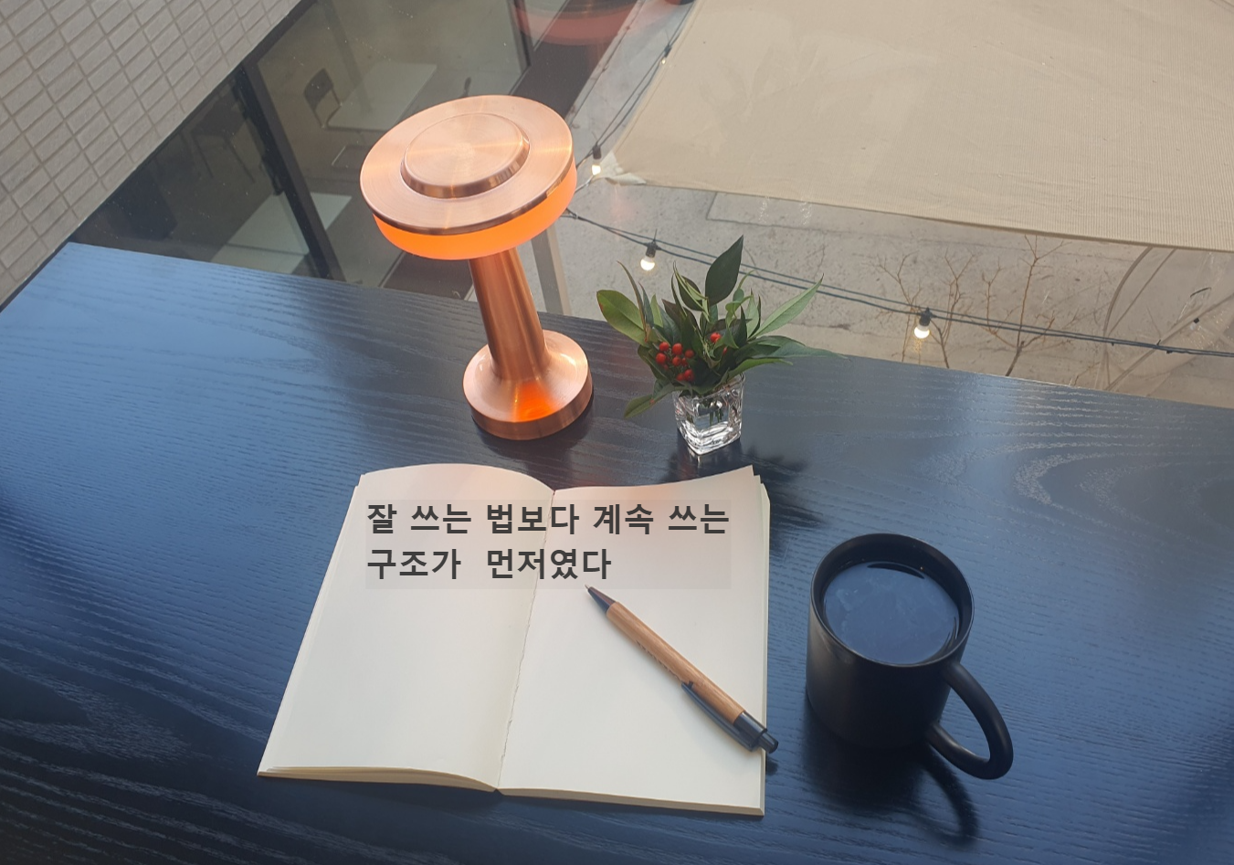 블로그 글쓰기 루틴을 기록하는 노트와 펜, 따뜻한 조명이 놓인 작업 공간 사진