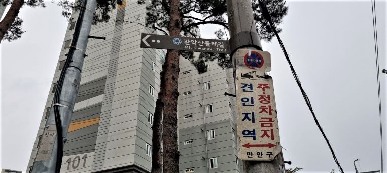 전신주에 붙은 관악산 둘레길 이정표, 뒤로는 고층거ㅗㄴ물, 올려다 본 사진, 주차금지 견인지역 경고문도 부착,