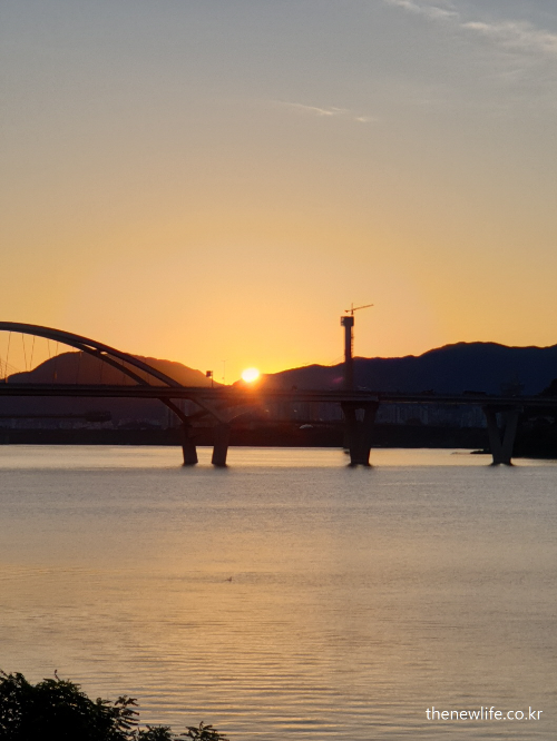 Sunrise behind Guri-Amsa Bridge over the Han River, symbolizing the awakening of the body and immune system through consistent morning walking.-한강 위 구리암사대교 뒤로 떠오르는 일출. 꾸준한 아침 걷기를 통해 몸과 면역력이 깨어나는 상징적인 장면.