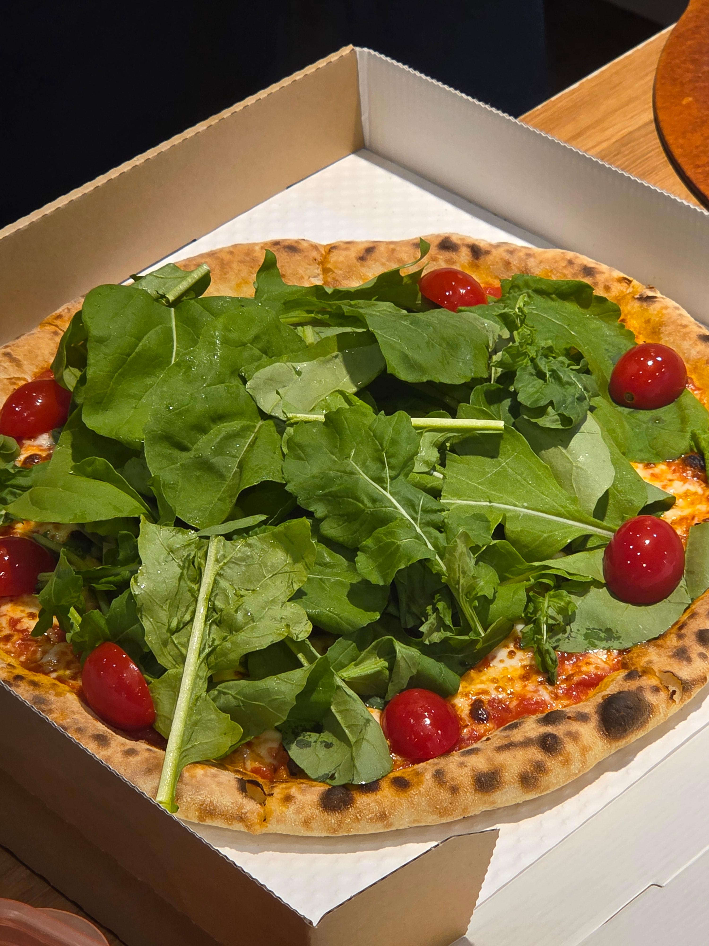 루꼴라와 방울토마토가 듬뿍 올려진 피자가 포장 박스 안에 담겨 있는 모습