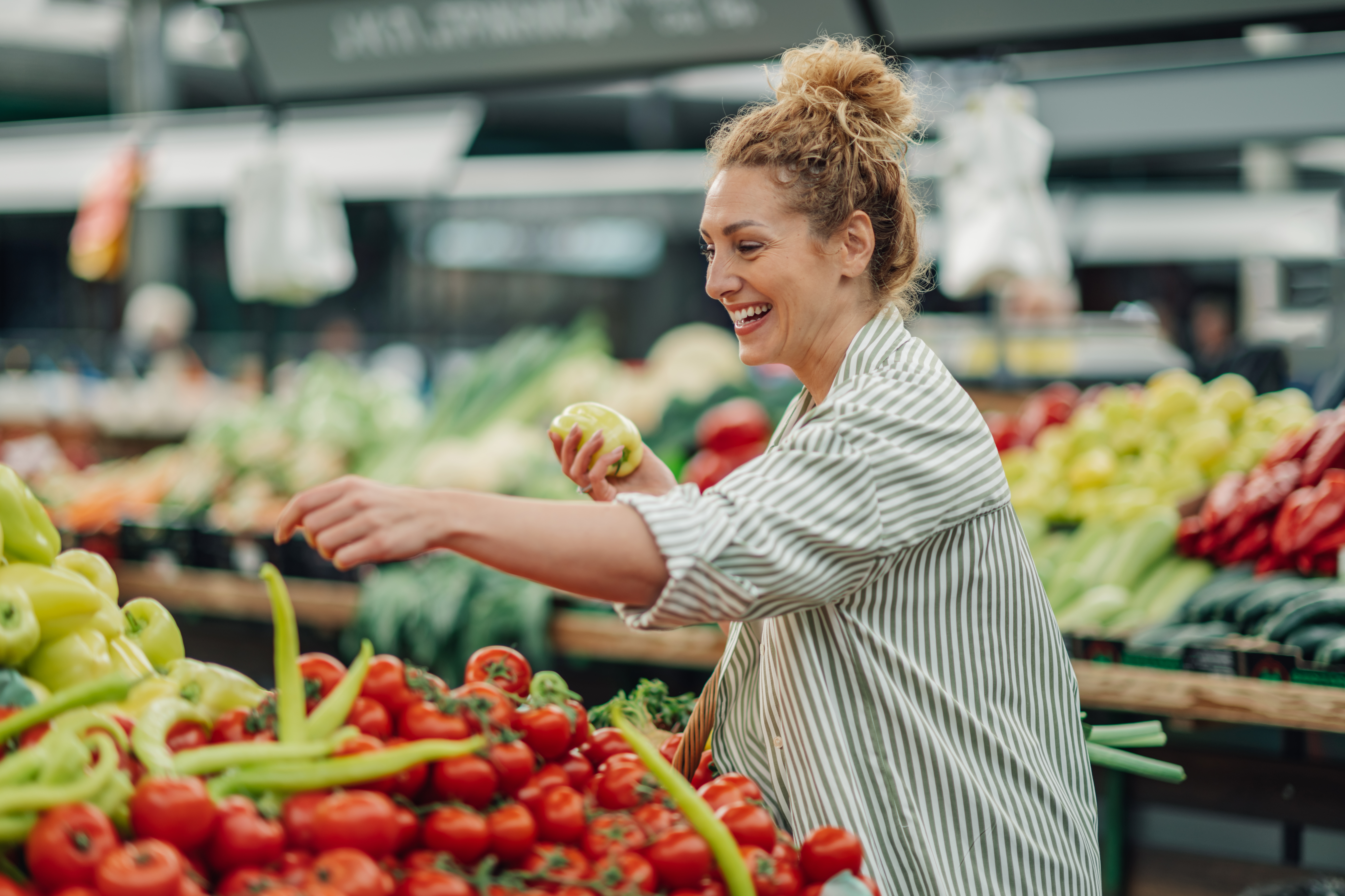 전통시장 채소 코너에서 웃으며 장을 보는 여성 – 정부 소비쿠폰 사용 가능 업종을 상징하는 이미지