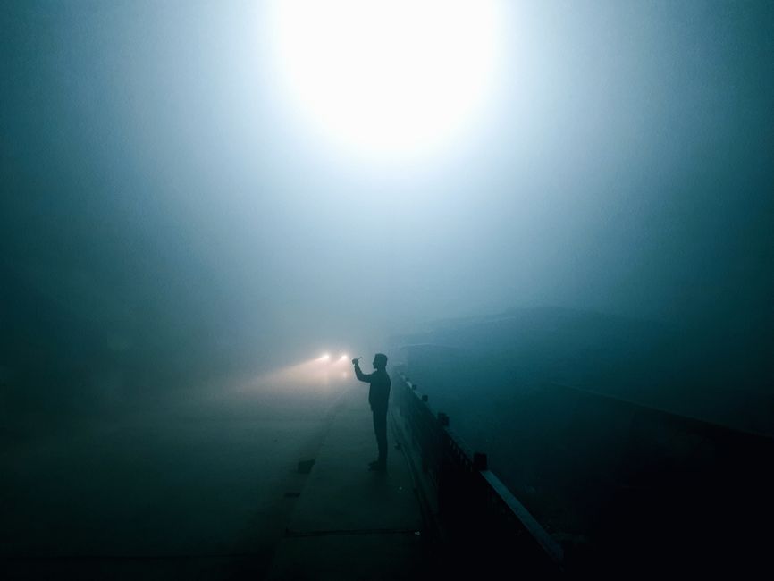 A person stands silhouetted on a foggy road at night, creating an eerie atmosphere.