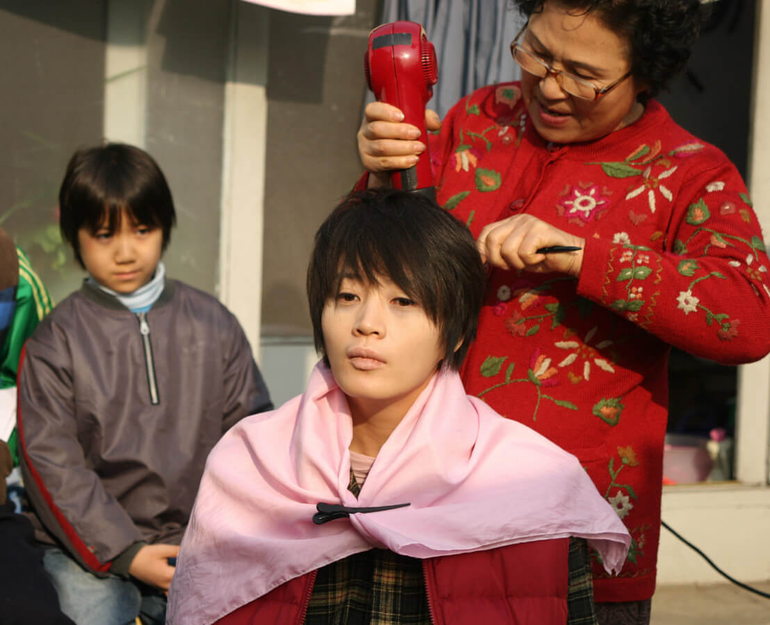 여자의 머리 드라이를 해주는 이웃집 할머니와 그들을 바라보는 재수