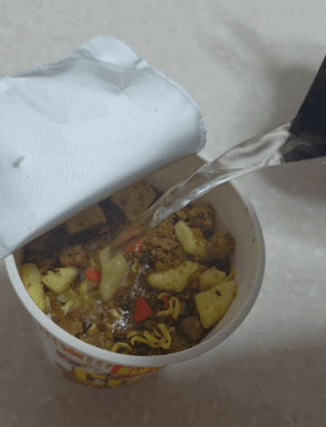 뚜껑을 살짝 연 일본 닛신 컵누들 카레맛에 뜨거운 물을 붓는 모습