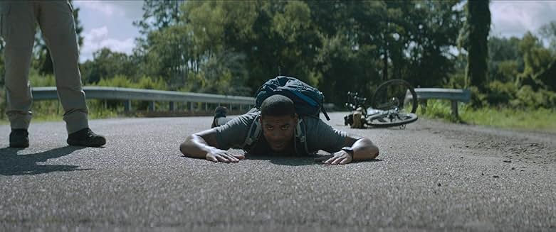 Rebel Ridge 영화 장면, 주인공이 도로 위에 엎드려 경찰에 제압당한 모습