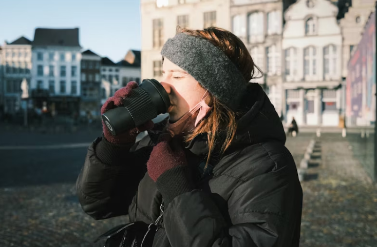 겨울 외출 중 따뜻한 음료를 마시는 여성, 보온 복장과 마스크를 착용한 모습