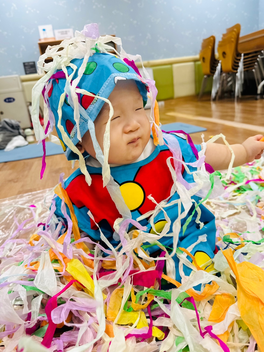 컬러풀한 습자지를 덮어쓴 채 윙크하는 듯한 표정의 9개월 아기