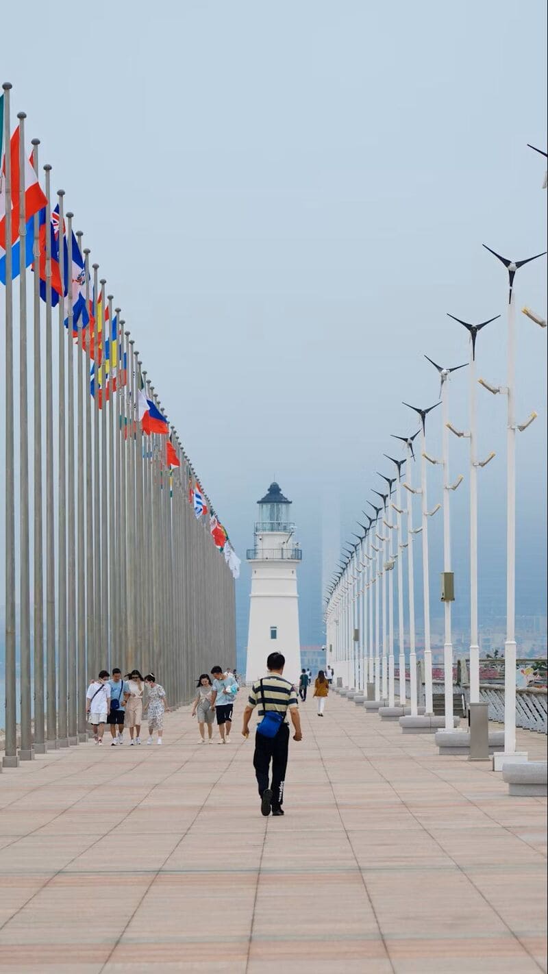 양쪽에 각국 국기가 펄럭이는 잔교 위를 사람들이 걷고 있고, 중앙에는 흰 등대가 우뚝 서 있는 장면