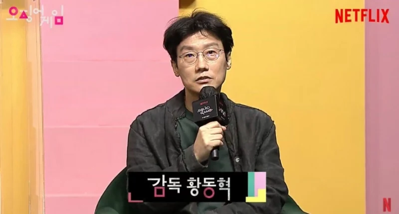 분홍색과 노랑색이 그려진 배경으로 인터뷰를 하고 있는 황동혁 감독