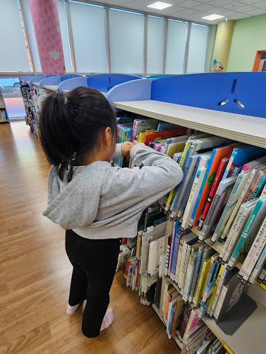 초등학생 아이가 도서관에 서서 책 고르는거 집중하고 있는 모습.