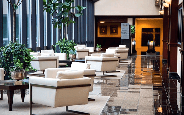 넓은 회사 로비 풍경이다. 하얀 소파들이 있고 식물을 심은 커다란 화분들도 많다. 천장엔 에어컨이 있다.