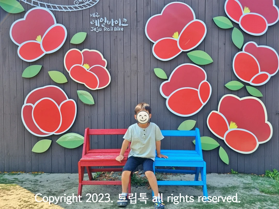 벽에 동백꽃 모양이 있고 의자에 아이가 앉아있다