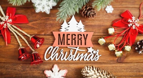 메리 크리스마스라고 적힌 글자가 나무 위에 놓여 있고 주위에 크리스마스 종등이 장식되어 있다.