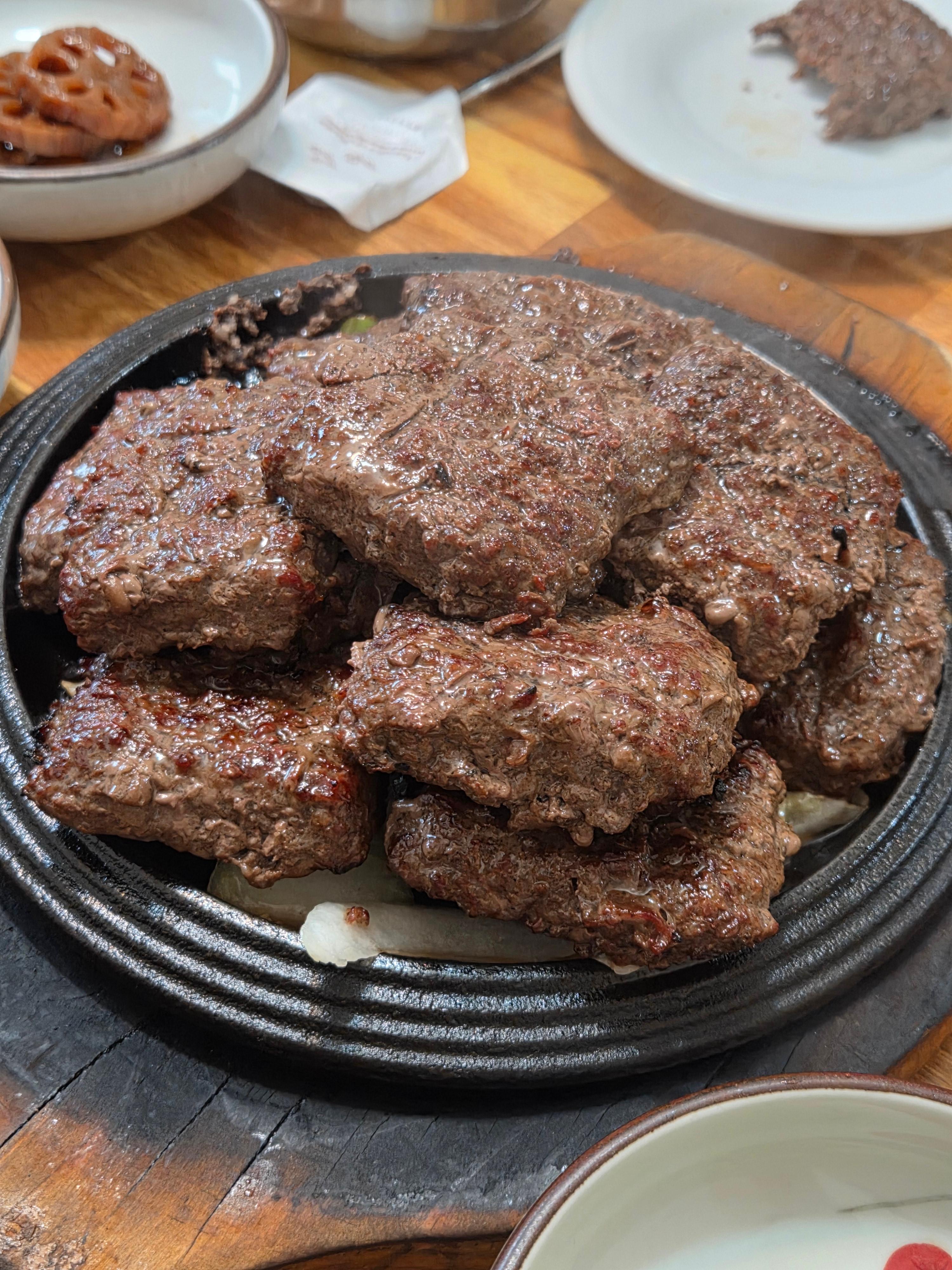 신식당 한우 떡갈비 구이 두툼한 다진 고기가 철판 위에 여러 개 올려져 김이 피어오르는 모습