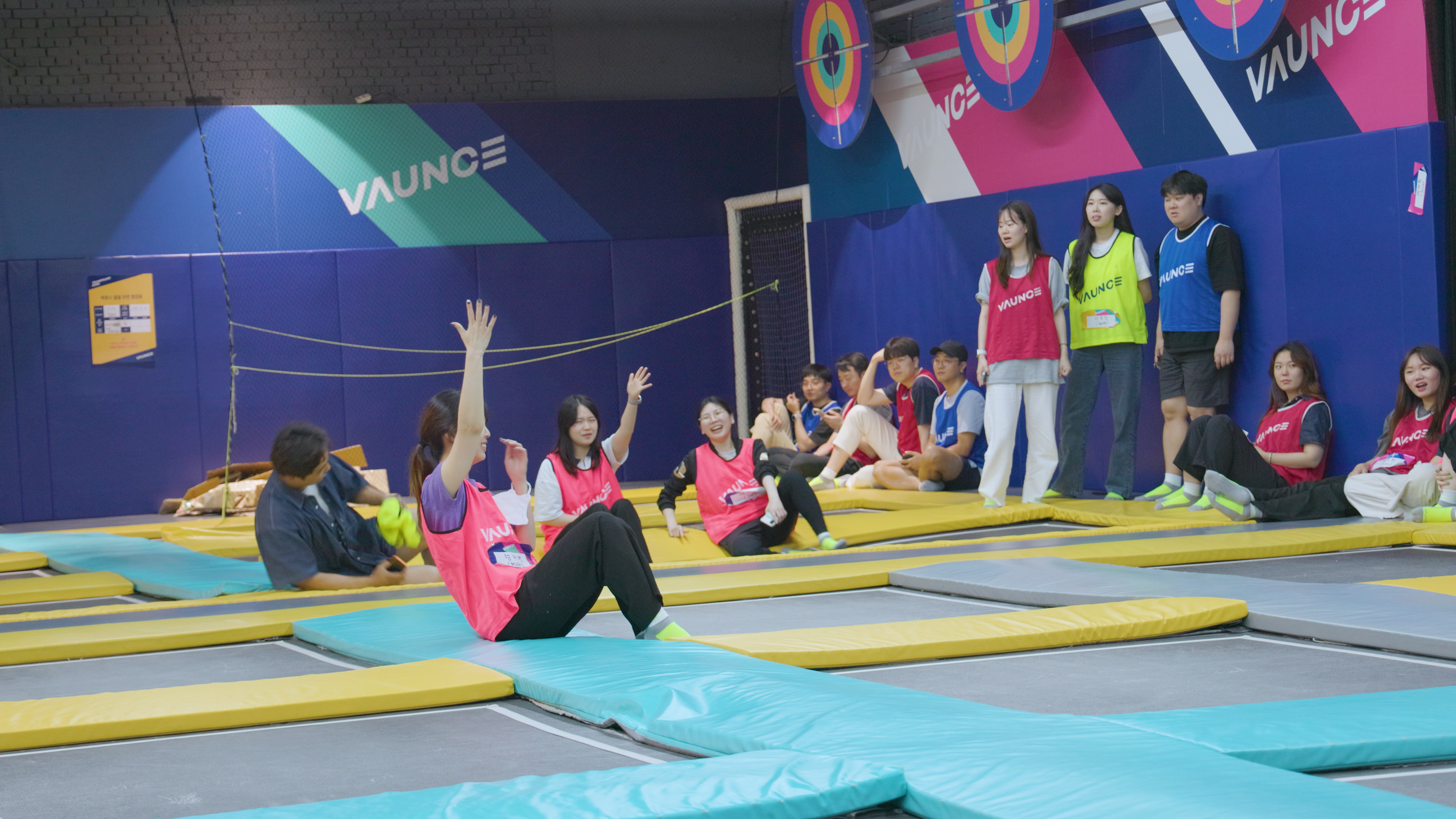 트램폴린 위에 앉아있는 사람들이 손을 공중에 뻗어 가위바위보를 하고 있다.