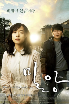 앞쪽에 서 있는 인물은 신애(전도연)의 표정은 담담하지만 슬픔을 담고 있고 뒤편에 종찬(송강호)이 서 있고, 잔잔한 도심과 해 질 무렵의 햇살이 보이며, 상단에 "비밀이 있습니다"라고 문구가 있음.