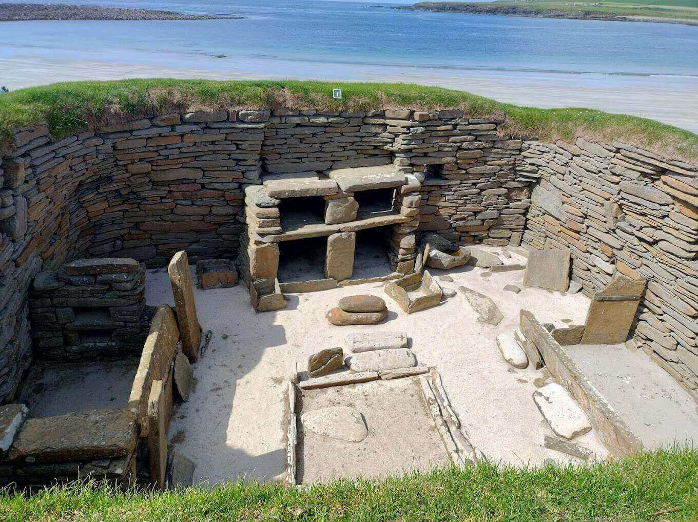 스카라 브레이 주거지 내부에 남아 있는 석조 침대와 벽장 구조. 배경에는 바다가 펼쳐져 있다.