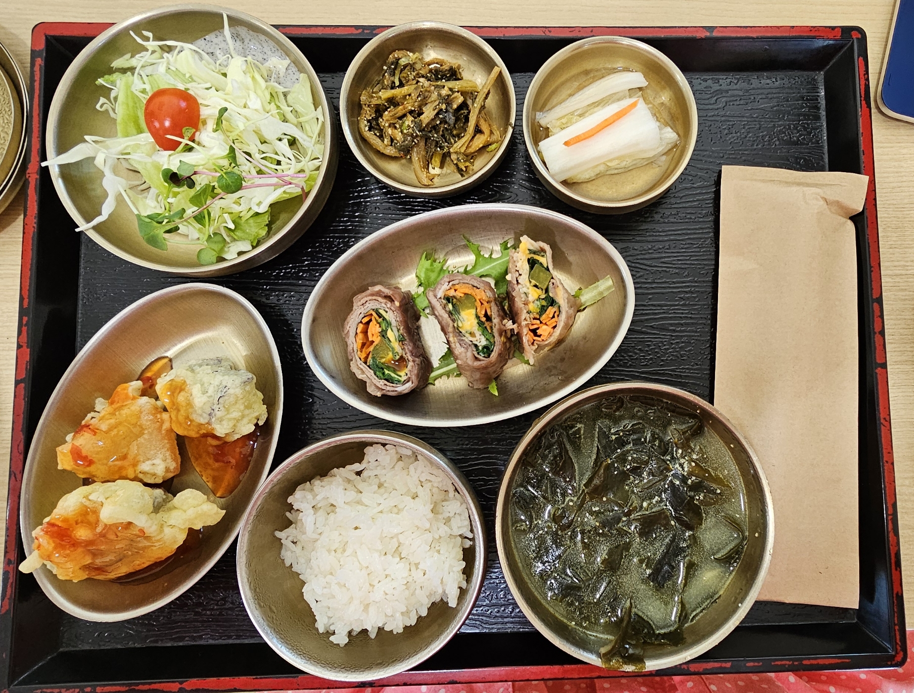 샐러드, 나물, 백김치, 가지튀김, 전병, 밥, 미역국이 올라가 있는 식판