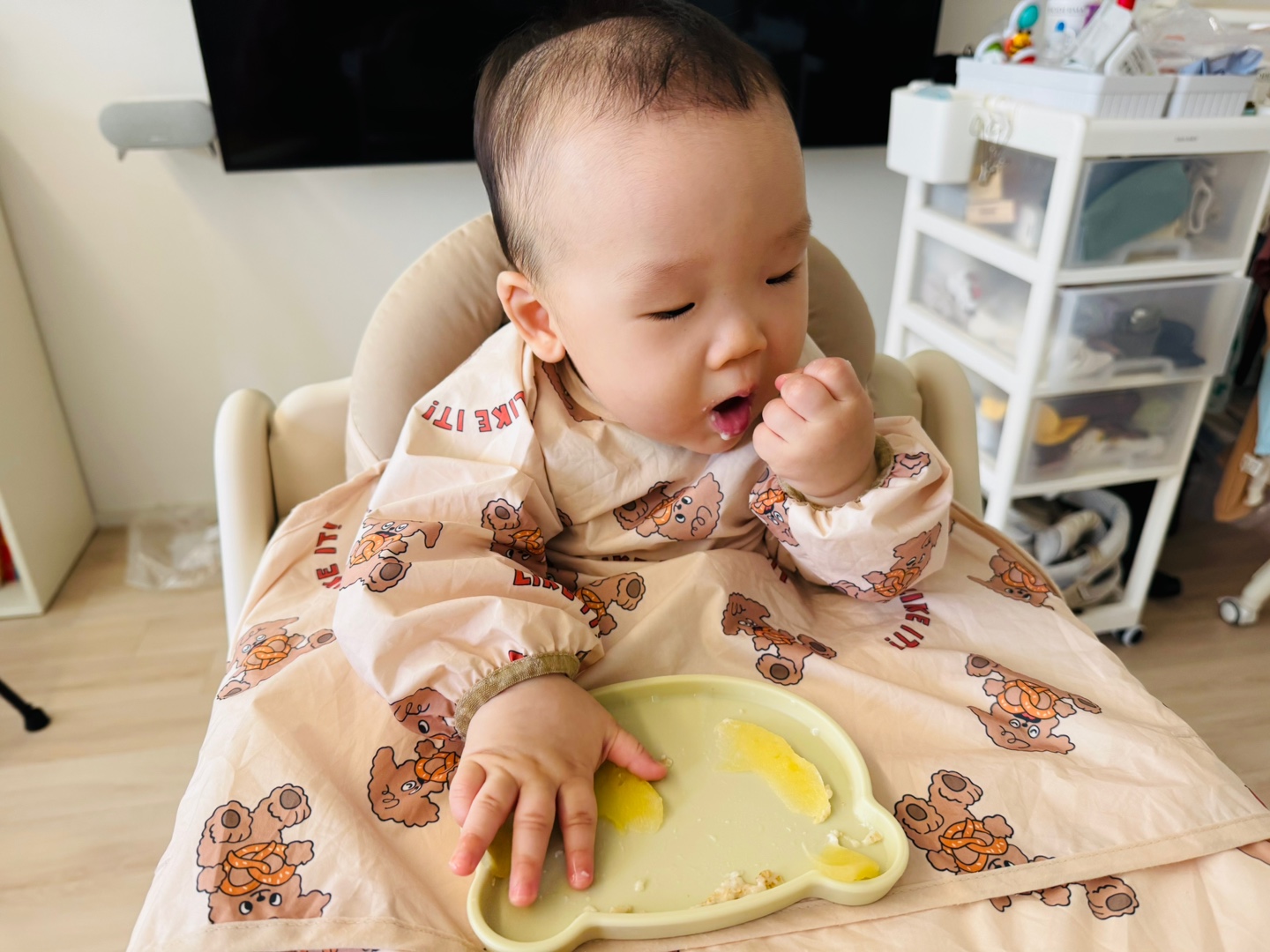 손에 사과를 쥐고 오트밀을 조심스럽게 떠먹는 9개월 아기의 모습