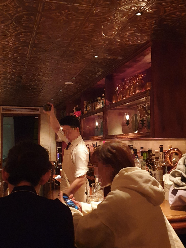 바텐더가 칵테일을 만들고 있다. 그 앞에서 이야기 중인 손님 2명