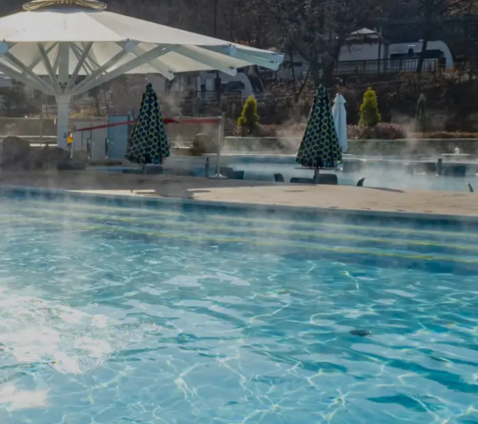 겨울방학 국내 여행지- 겨울 흰눈이 쌓인 초록 숲 앞 연기가 나는 수영장