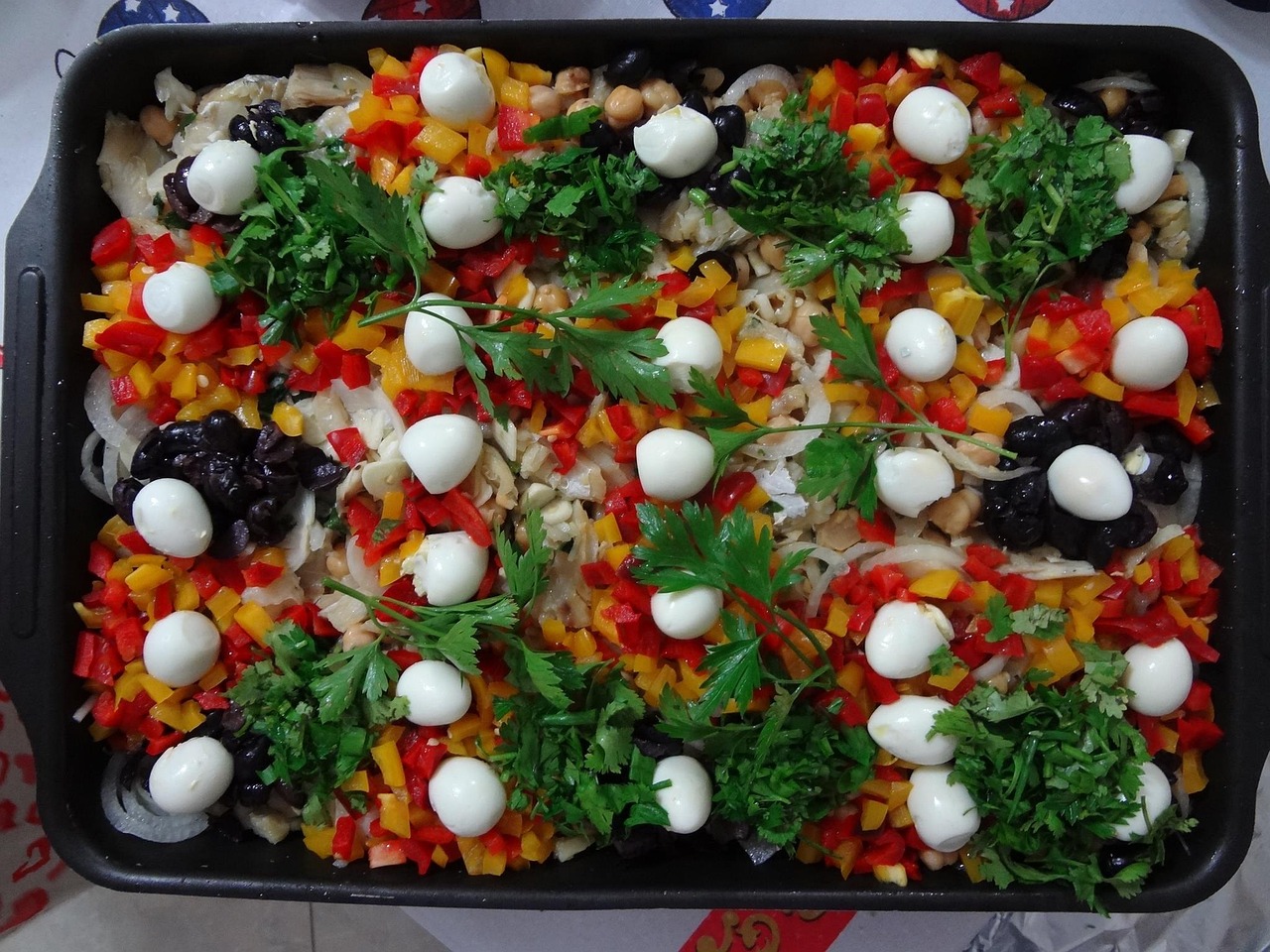 사각혛의 오븐 그릇 안에 다진 파프리카위에 올려진 삶은 메추리알들과 병아리콩이 가득 있다.