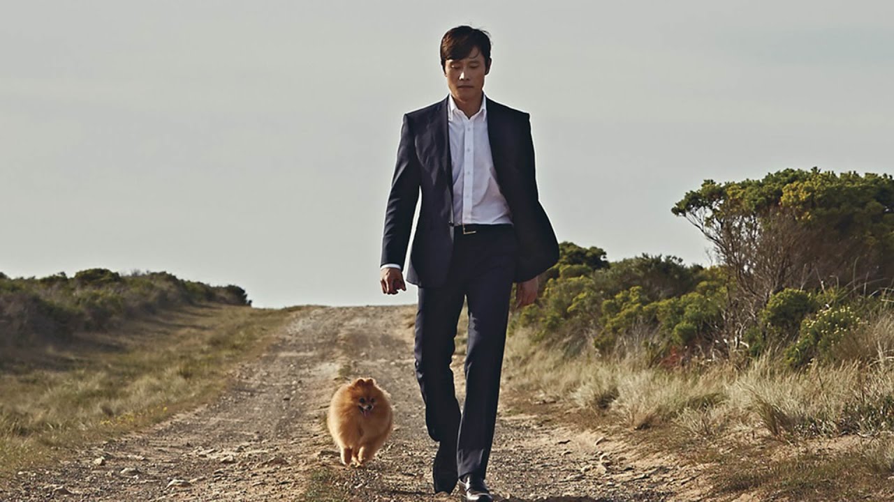 정장을 입은 주인공이 작은 개와 함께 외딴 길을 걷는 장면, 영화 싱글라이더 포스터