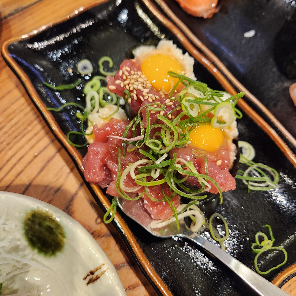 참치 회 위에 메추리알 노른자와 깨 그리고 가늘게 썬 파가 올려져 있다.